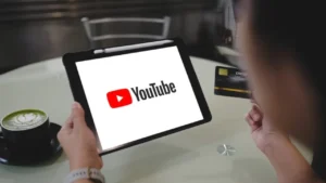 Person holding a tablet with YouTube logo and credit card in hand
